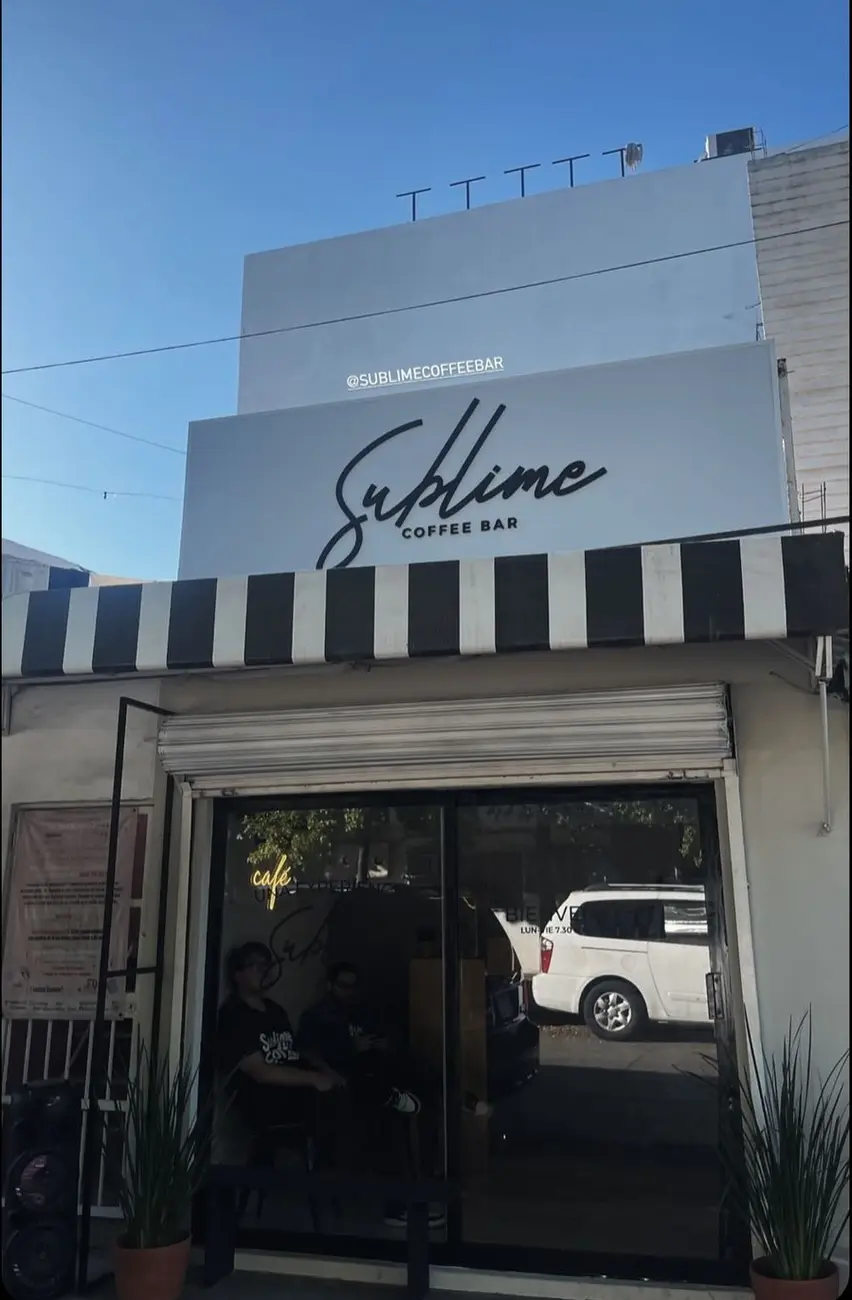 La fachada de Sublime Coffee Bar: letrero blanco con su logo y el toldo de rayas negras y blancas sobre la puerta de vidrio