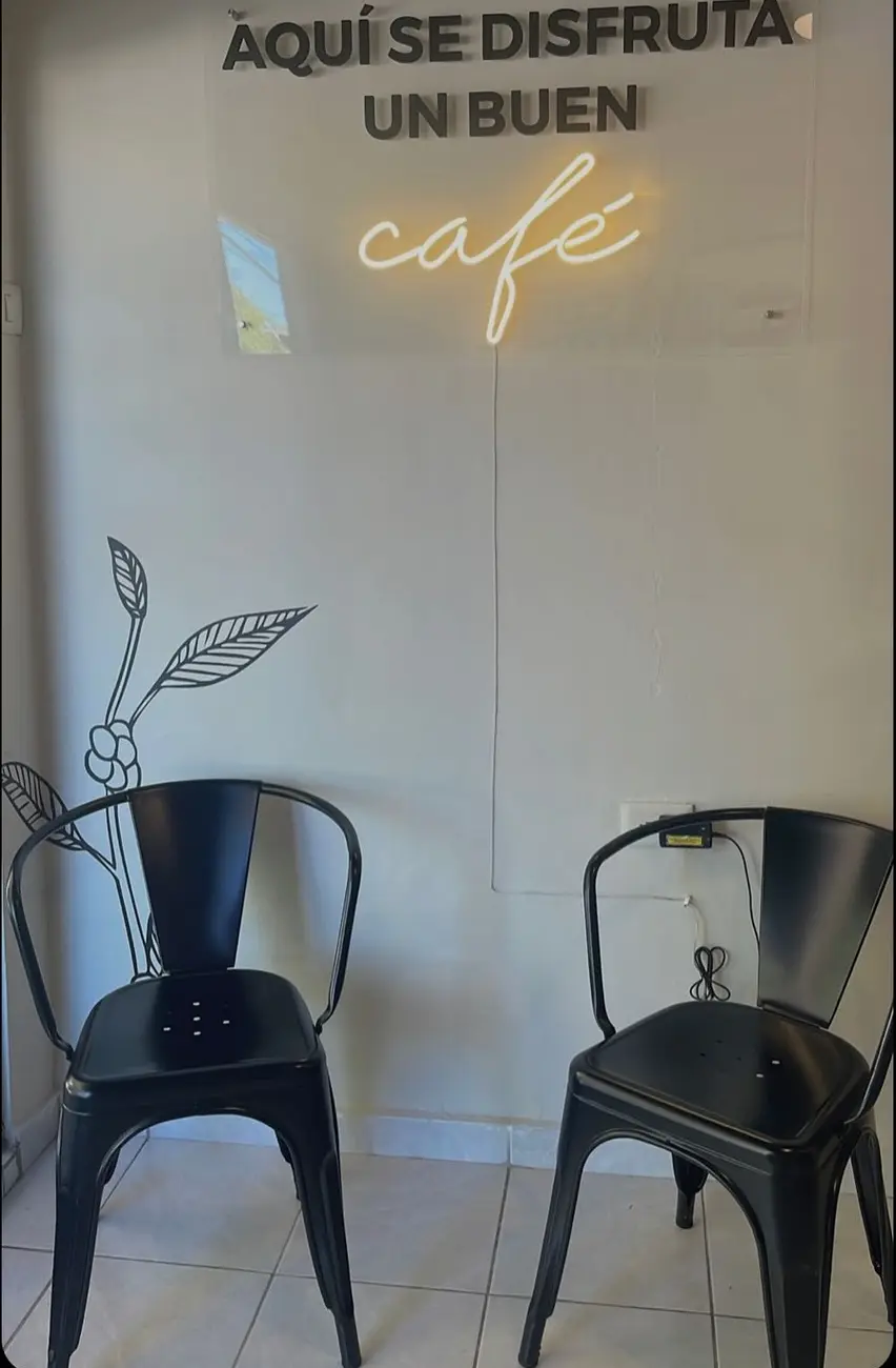 El neón Aquí se disfruta un buen café sobre la pared blanca de Sublime, con dos sillas negras